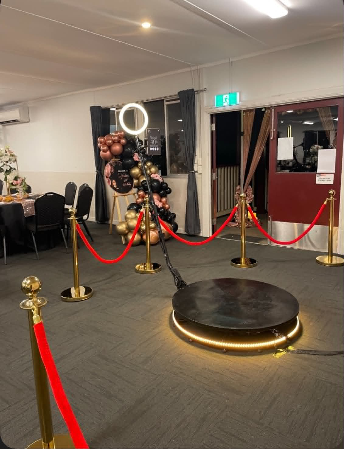 360 photo booth setup with red ropes, gold bollards and balloon backdrop at an indoor event
