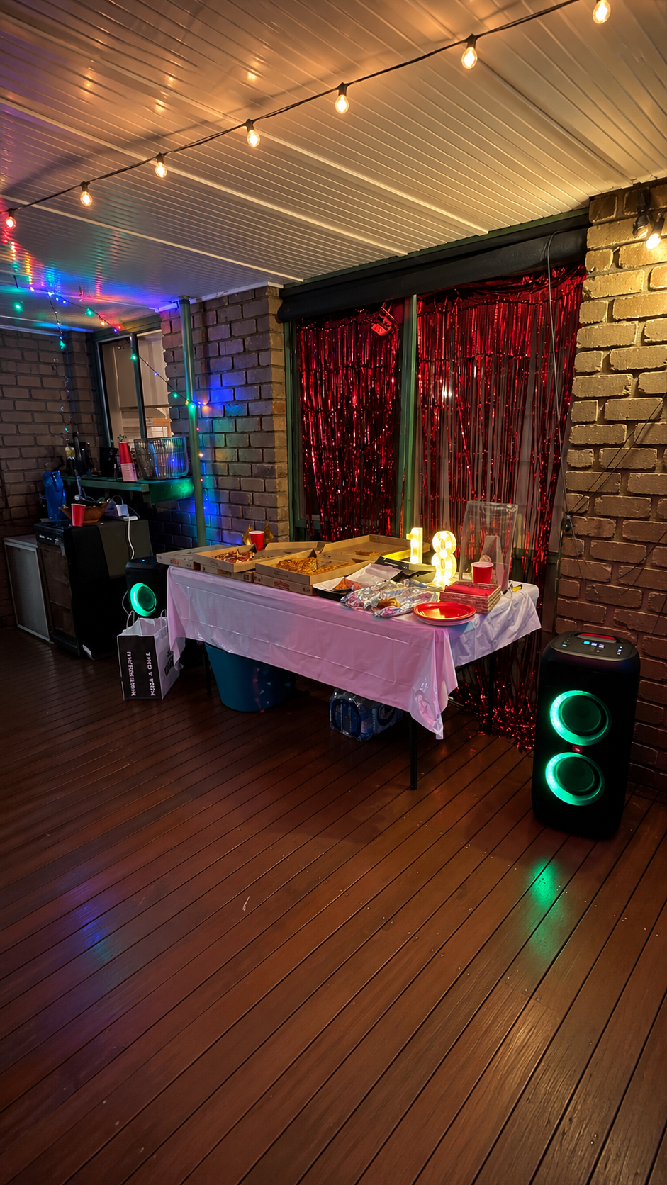Birthday setup with twin party speakers, string lights and red shimmer backdrop