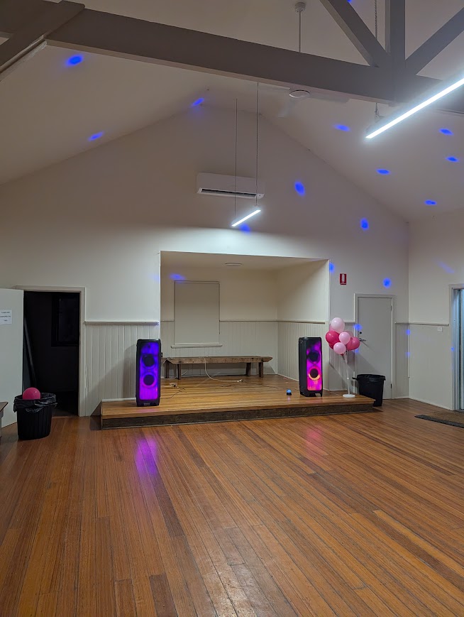 Two party speakers on the stage of a timber community hall with blue lighting